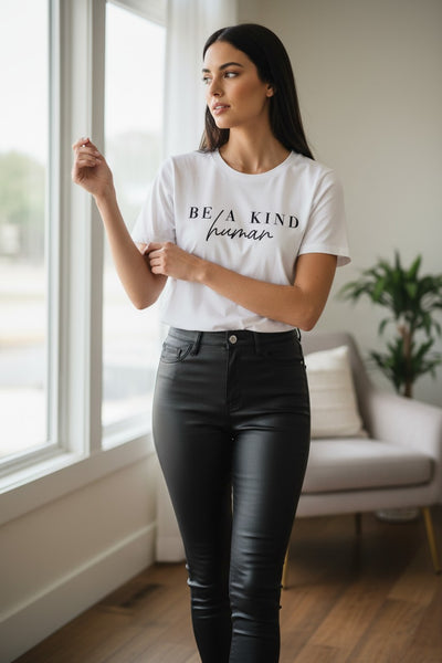 Woman wearing a white t-shirt with 'Be a Kind Human' text in a room with a couch and plant.