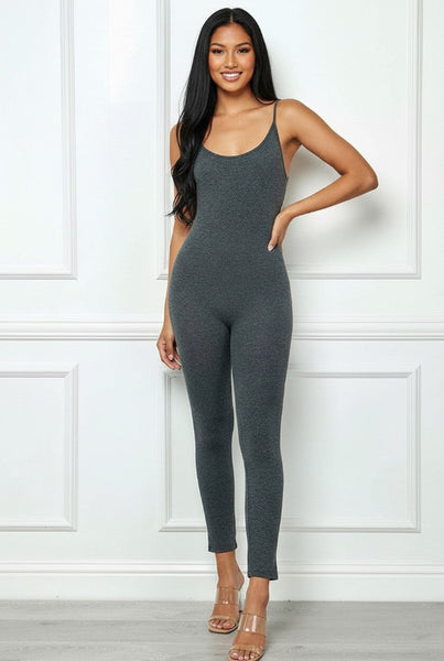 Woman wearing a gray jumpsuit against a white paneled wall.