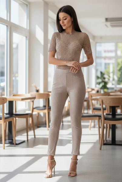 Woman in taupe faux suede fitted pants standing in a modern cafe with large windows.