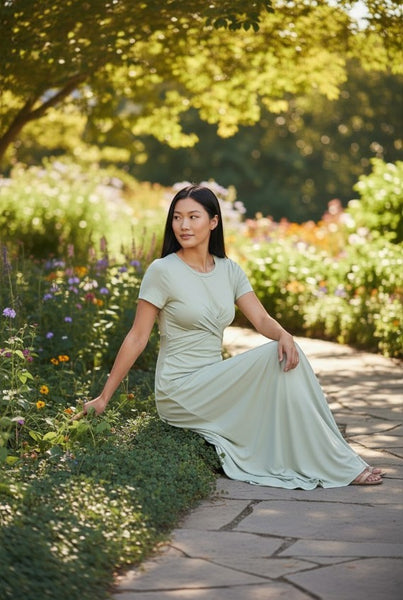 Collab Boutique light green rayon spandex crew neck maxi dress with short sleeves and twisted waist detail, worn by a model sitting in a garden.