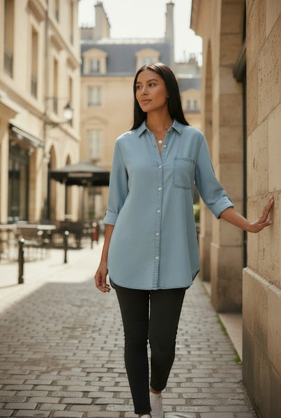 Collab Boutique light blue Tencel denim shirt with button sleeves and a chest pocket, worn by a woman walking outdoors.
