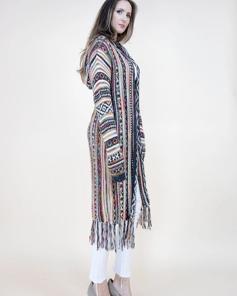 Collab Boutique longline hooded knit cardigan with geometric tribal pattern and fringed hem in multi-color. Model wears white jeans.