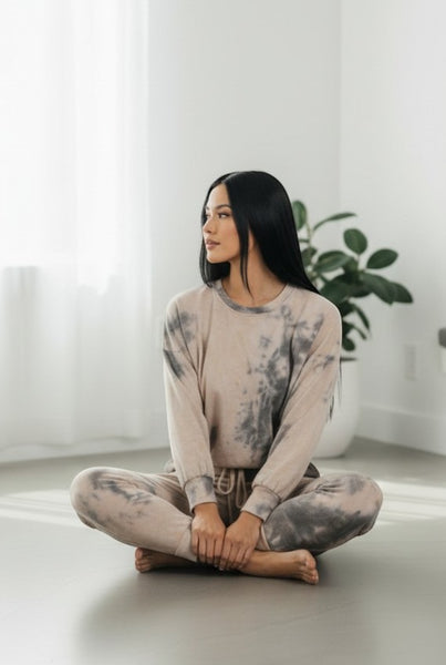 Collab Boutique neutral tie-dye lounge set on a woman sitting cross-legged. Made of polyester, rayon, and spandex.